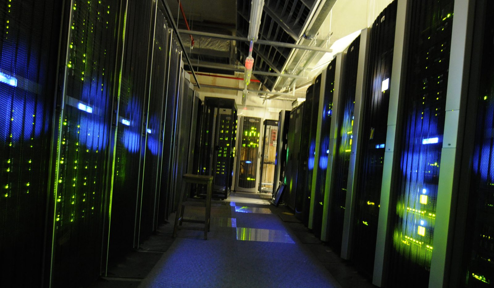 Pasillo de una sala de servidores con racks activos iluminados en azul y verde, la infraestructura técnica real que hay que inventariar y proteger en una auditoría de ciberseguridad