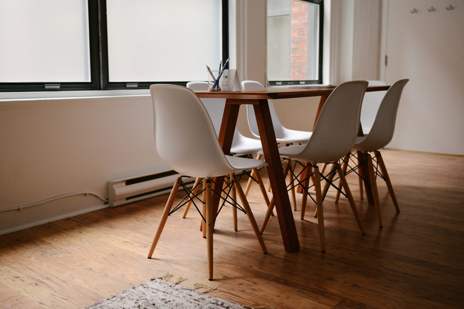 Sala de reuniones vacía y minimalista con mesa de madera clara, sillas blancas y paredes neutras iluminada por luz natural, preparada para una reunión de revisión del sistema de gestión